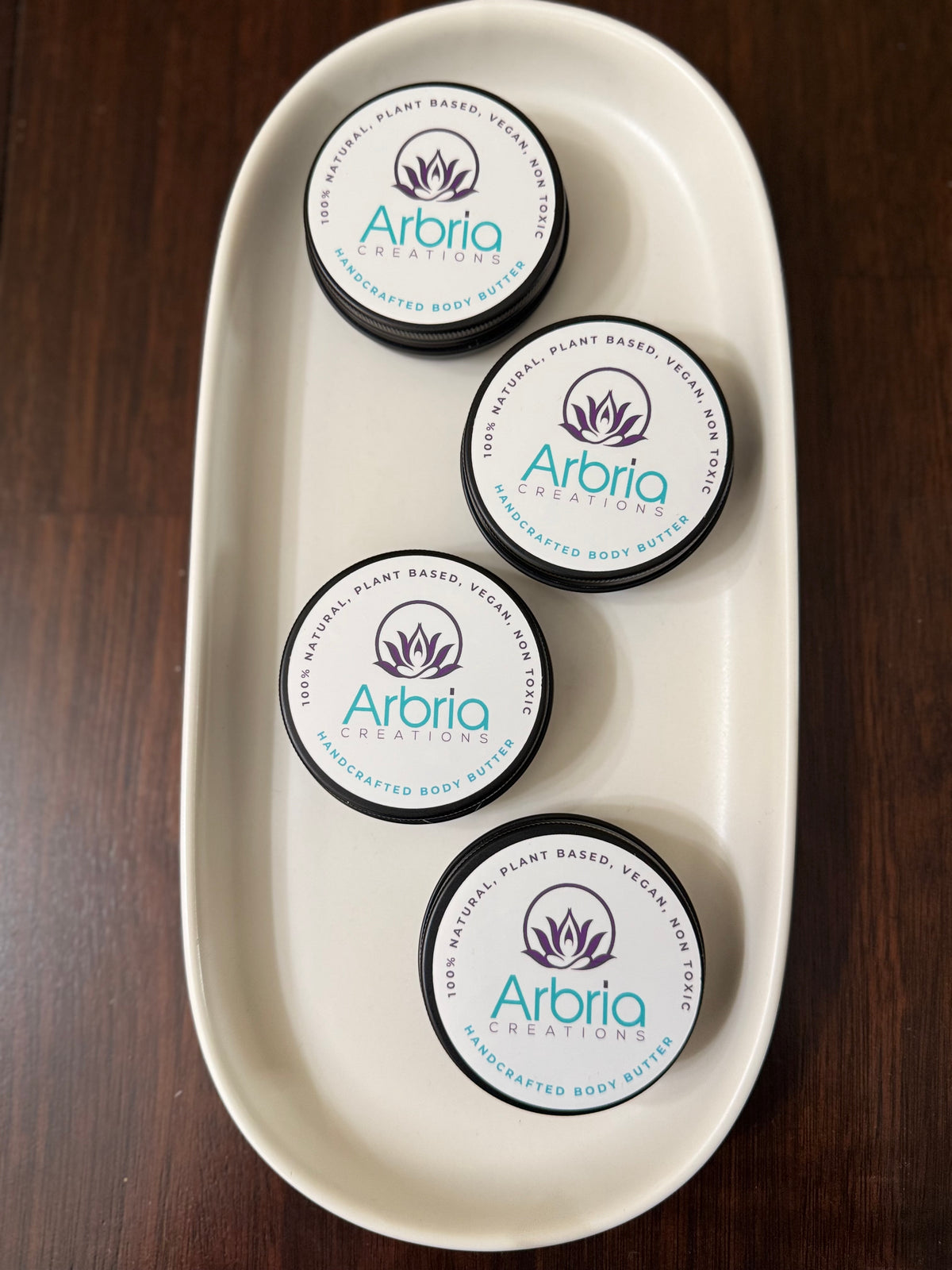 Four Arbria Creations 2 oz mini whipped body butter jars arranged in a white oval tray