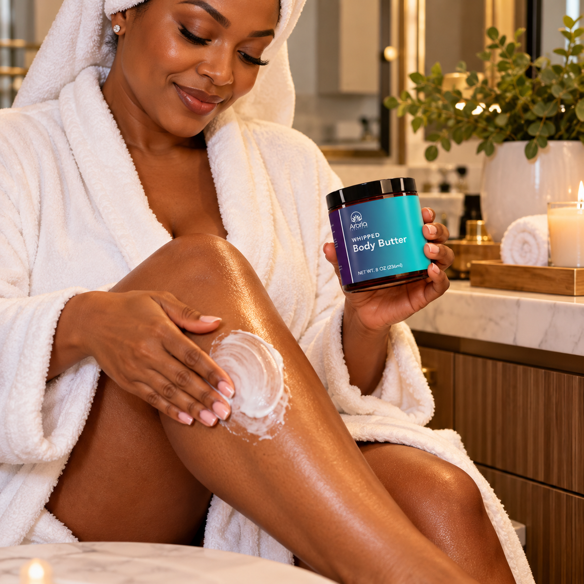 A woman in a white bathrobe applies body butter cream to her leg while holding a jar of 'Pleasanton' 'Healing Body Butter' in a bathroom setting.